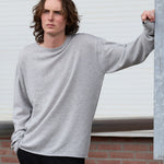 man wearing a grey cashmere crew-neck sweater and black pants standing on the pavement.