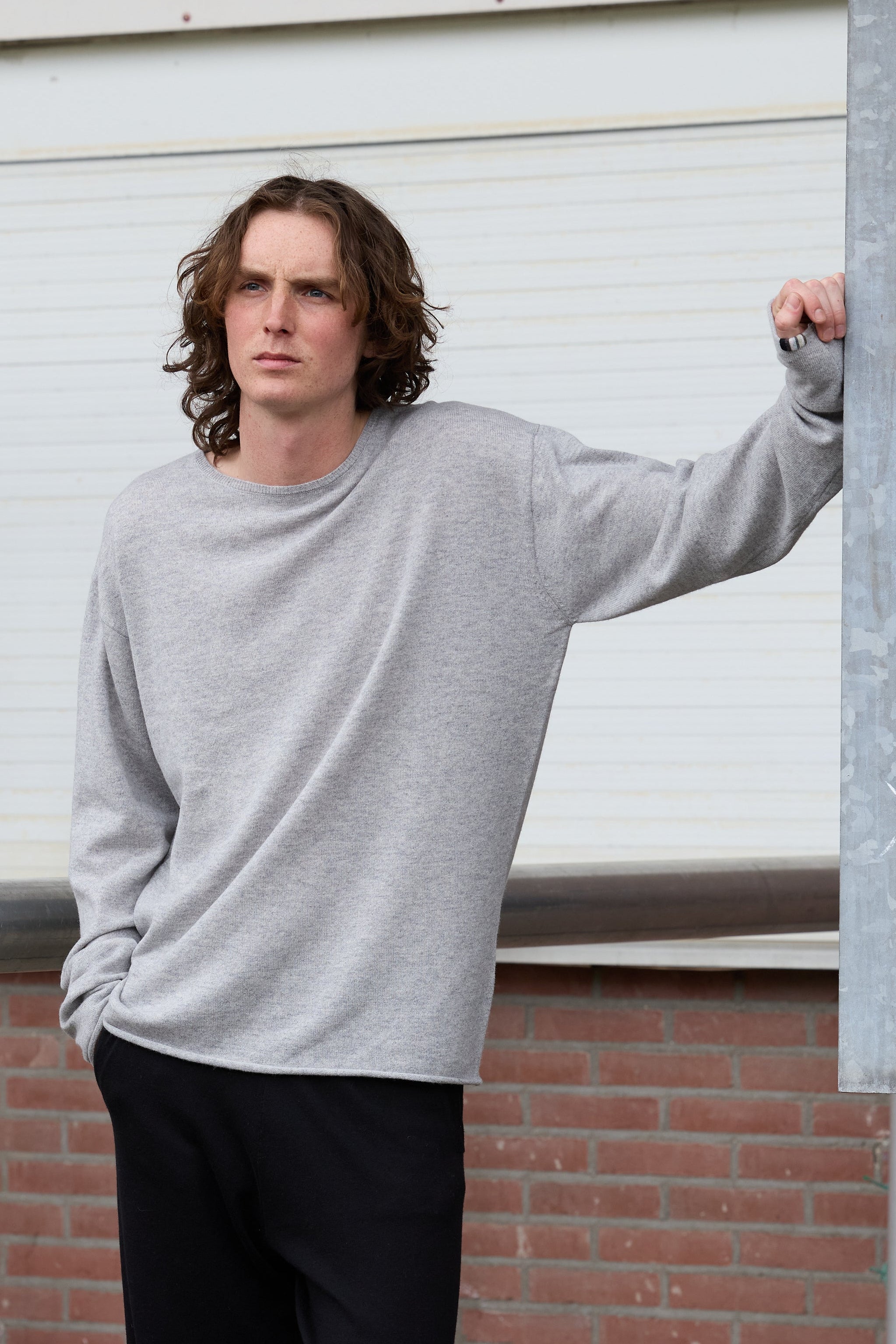 man wearing a grey cashmere crew-neck sweater and black pants standing on the pavement.