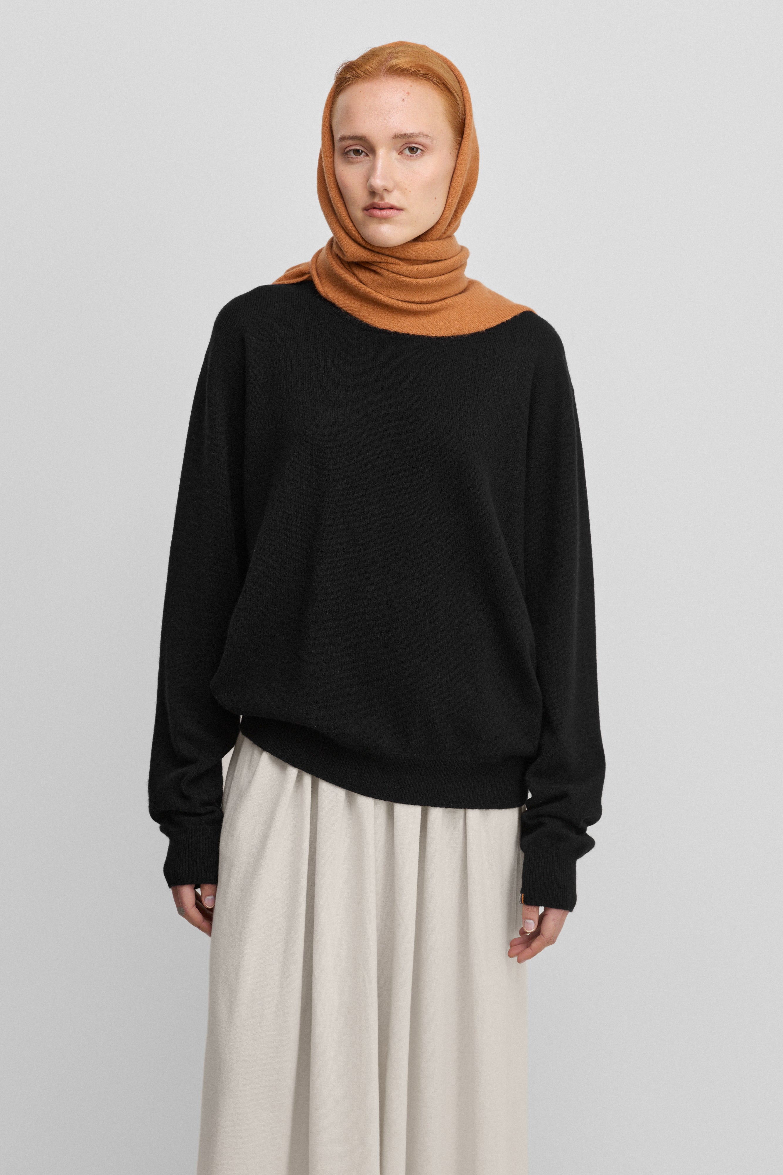 woman wearing a black loose-fit cashmere crew-neck sweater with ribbed trims, styled with a white skirt.