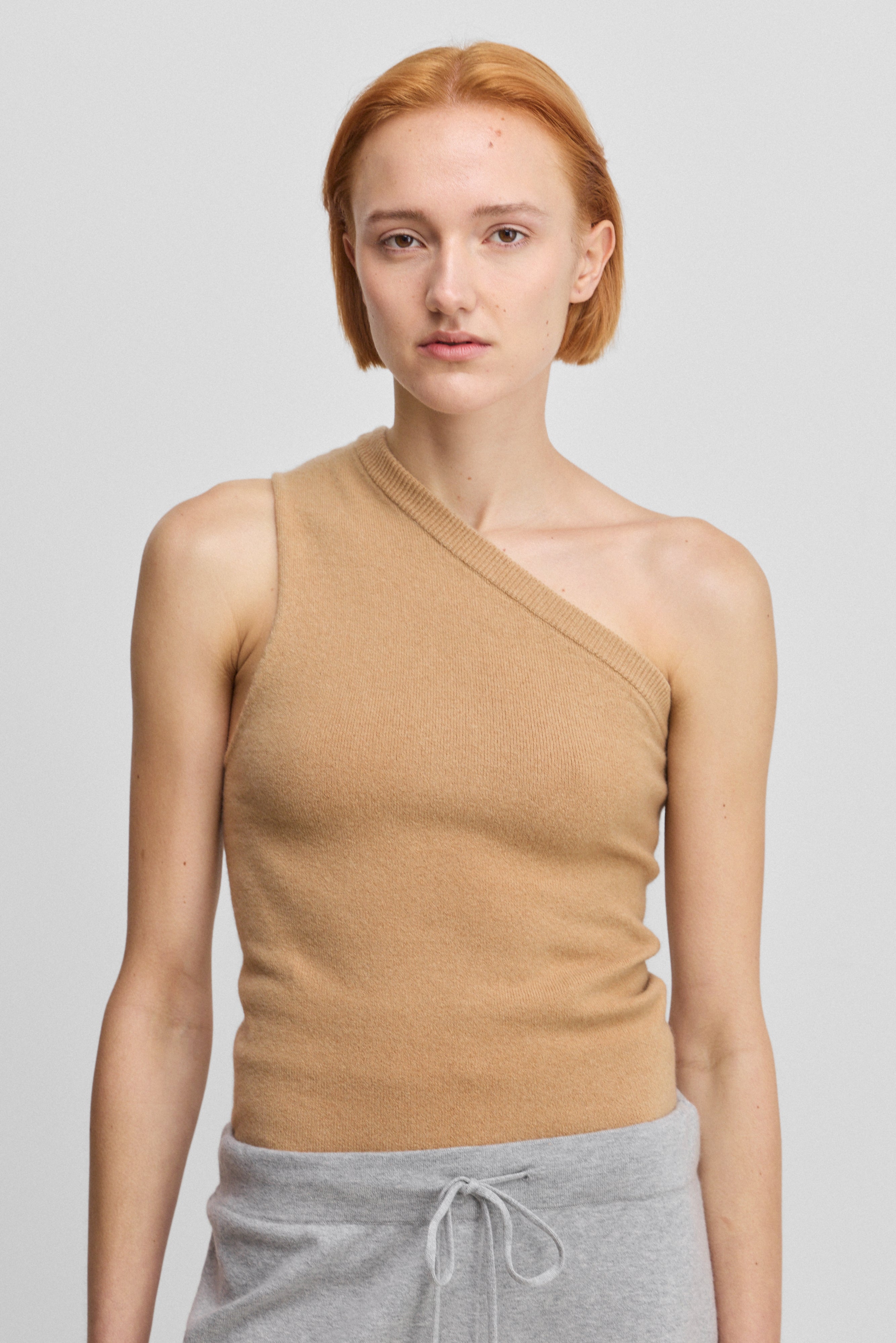 woman wearing a camel beige fitted one-shoulder cashmere top.