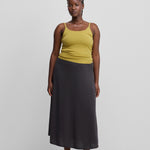 woman wearing a yellow fitted cotton cashmere strap top, styled with a grey skirt.