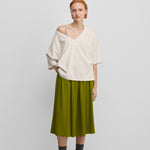 woman wearing an oversized white cotton cashmere v-neck t-shirt with elbow-length sleeves, styled with a green skirt.