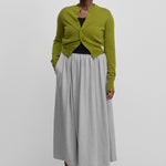 woman wearing a long grey cotton cashmere skirt with an elasticated waistband, styled with a green cardigan.