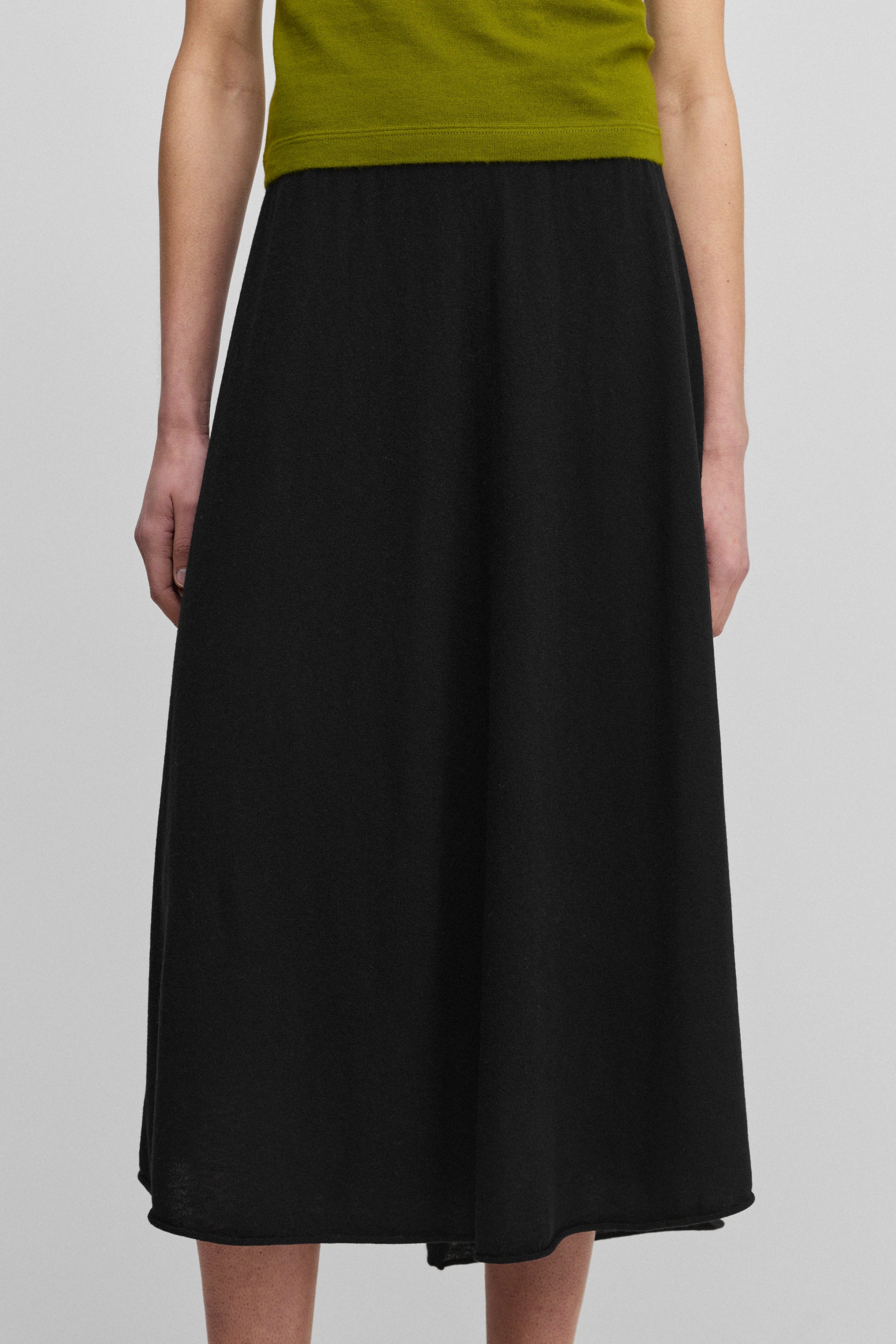 woman wearing a black wool cashmere midi skirt with a rib-knitted waist and a rolling edge hem.