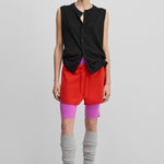 woman wearing a black sleeveless cotton-cashmere button-up vest, styled with red shorts.