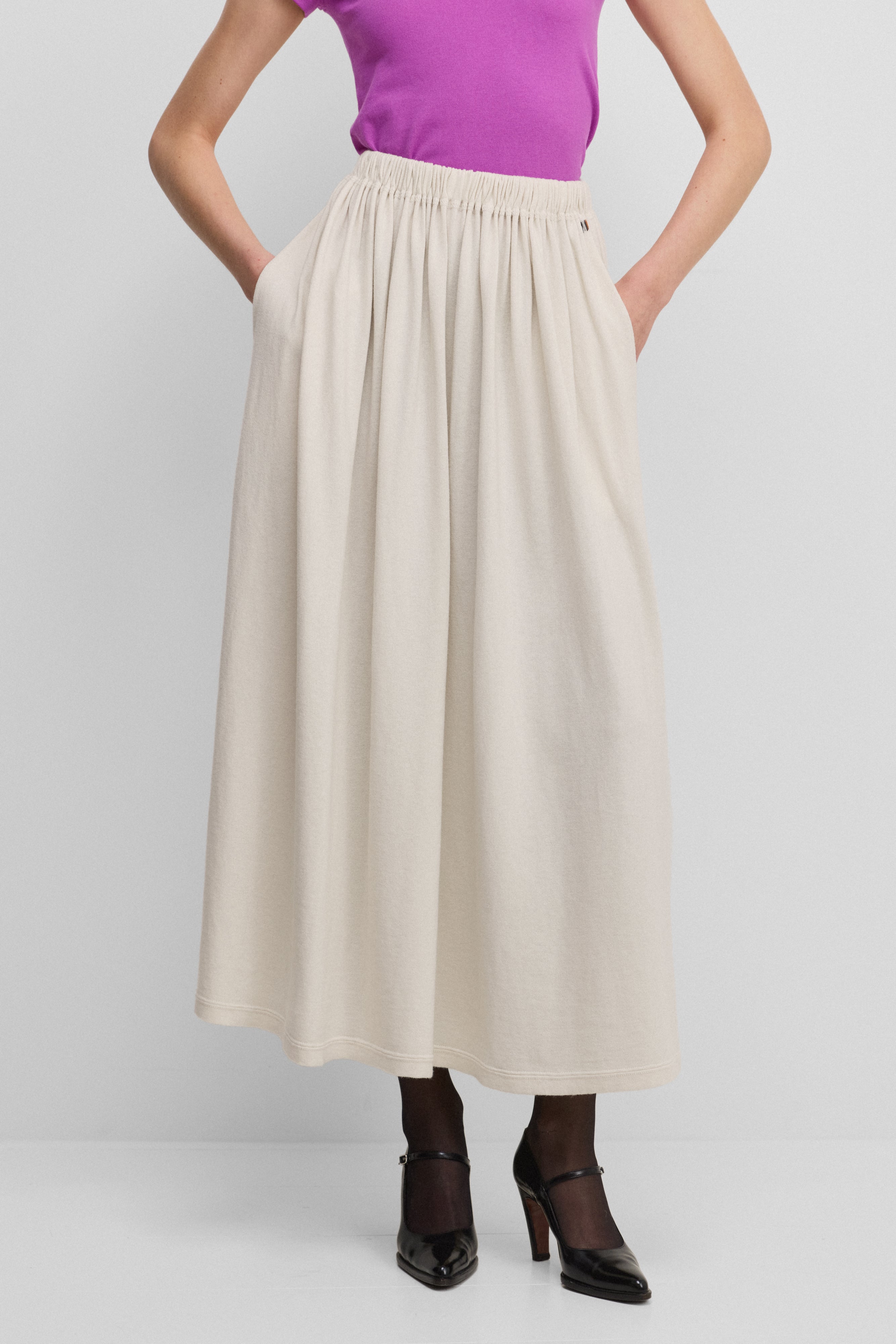 woman wearing a long off-white gathered cotton cashmere skirt with an elasticated waistband and two side pockets.