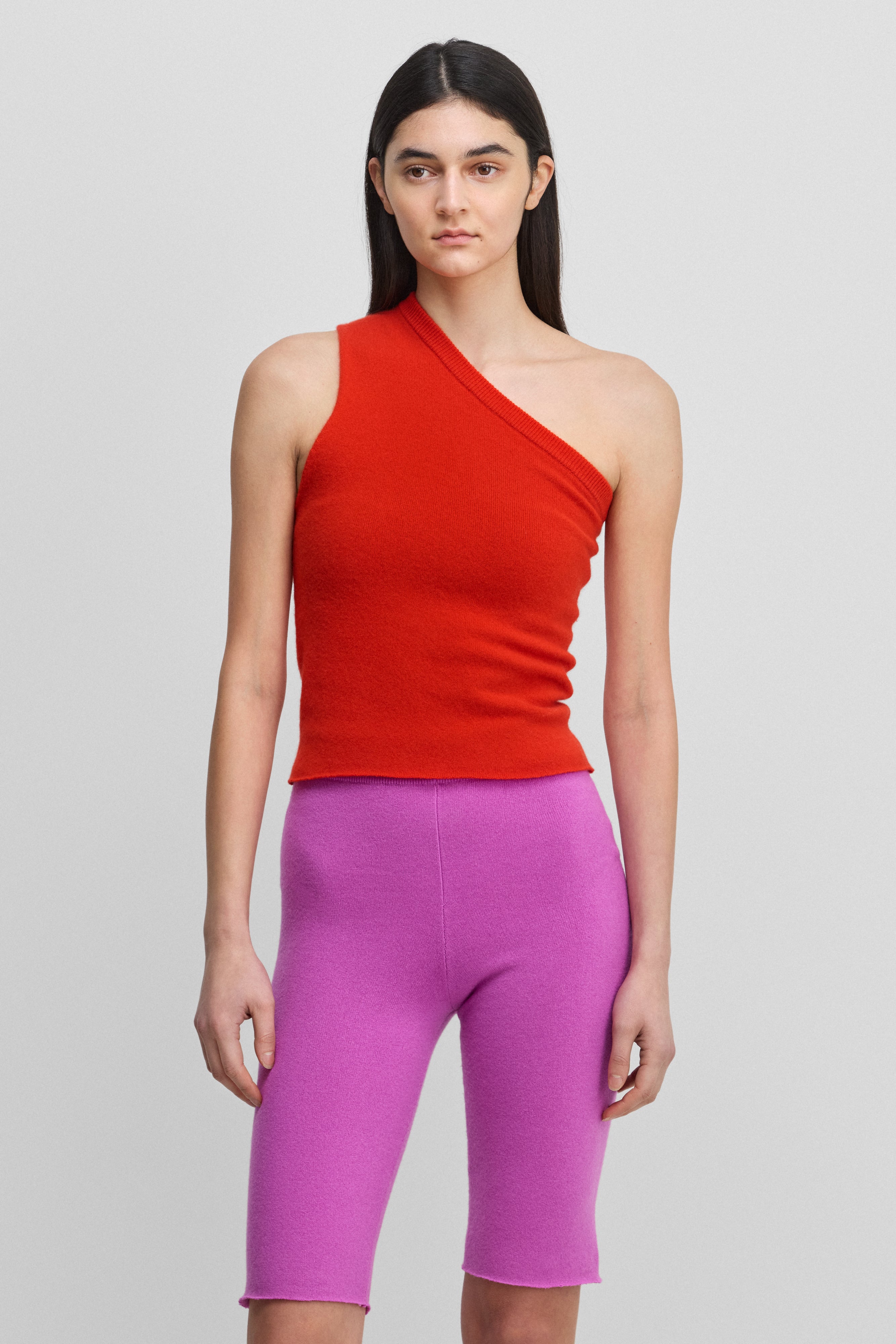 woman wearing a bright red fitted one-shoulder cashmere top.