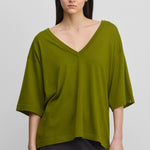 woman wearing an oversized green cotton cashmere t-shirt with a deep v-neck and elbow-length sleeves.