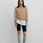 woman wearing a camel beige cashmere button-up cardigan with a rib-knitted collar, styled with black biker shorts.