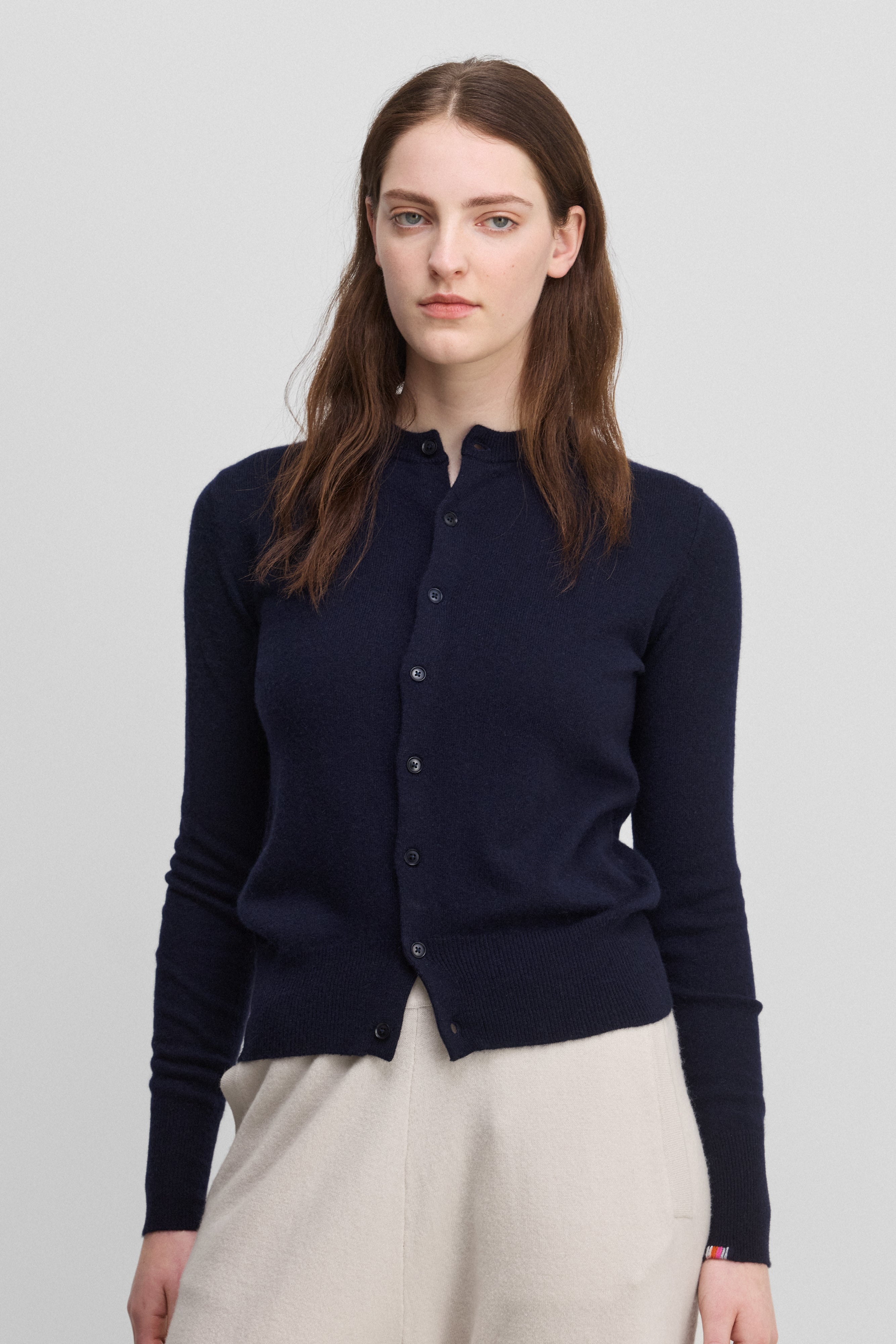 woman wearing a navy blue cashmere crew-neck cardigan with eight corozo buttons and ribbed trims.