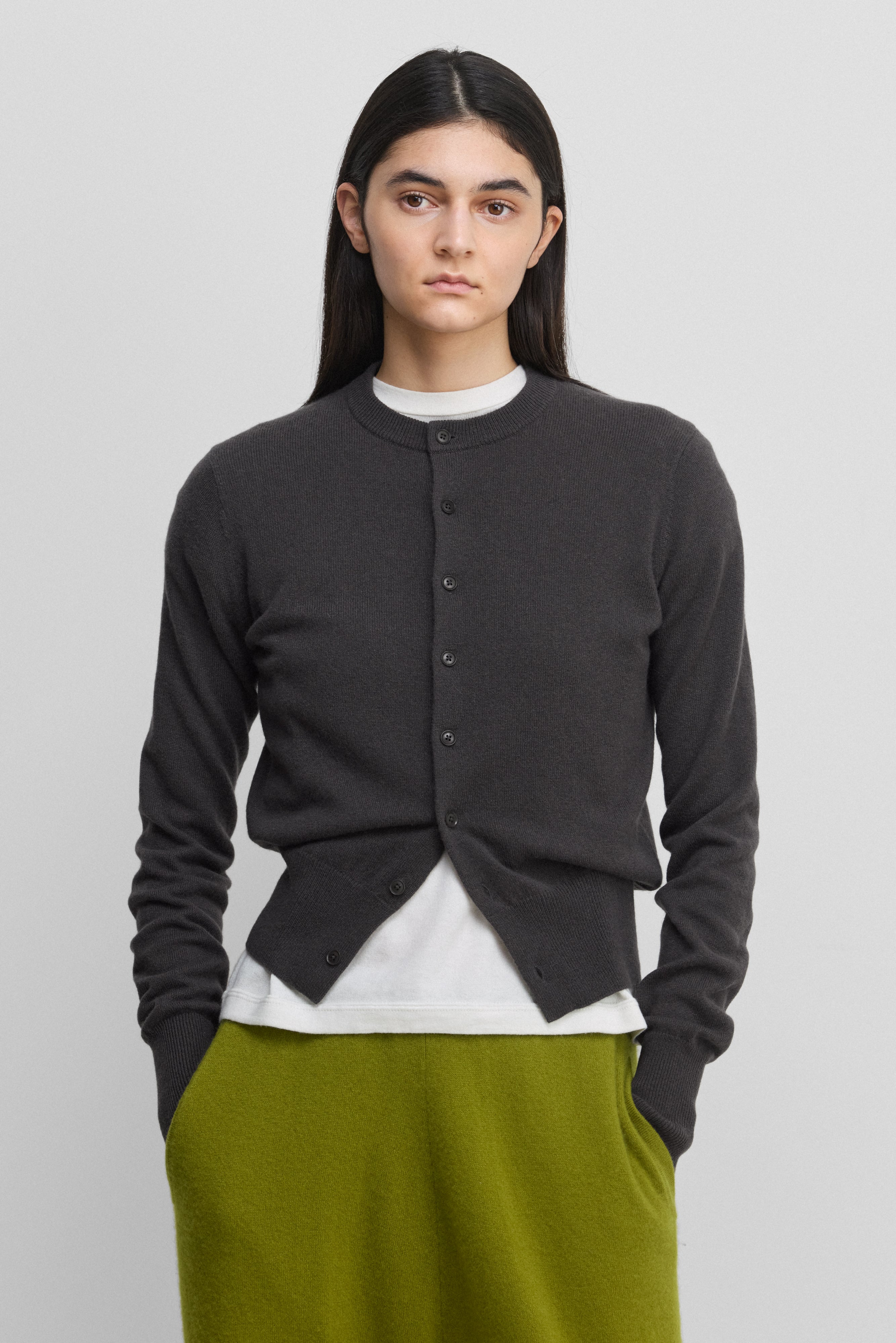 woman wearing a dark grey cashmere crew-neck cardigan with eight corozo buttons and ribbed trims.