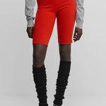 woman wearing black rib-knit cashmere leg warmers, styled with red biker shorts.