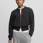 man wearing a dark grey cashmere crew-neck cardigan with a metallic two-way zipper and side pockets.