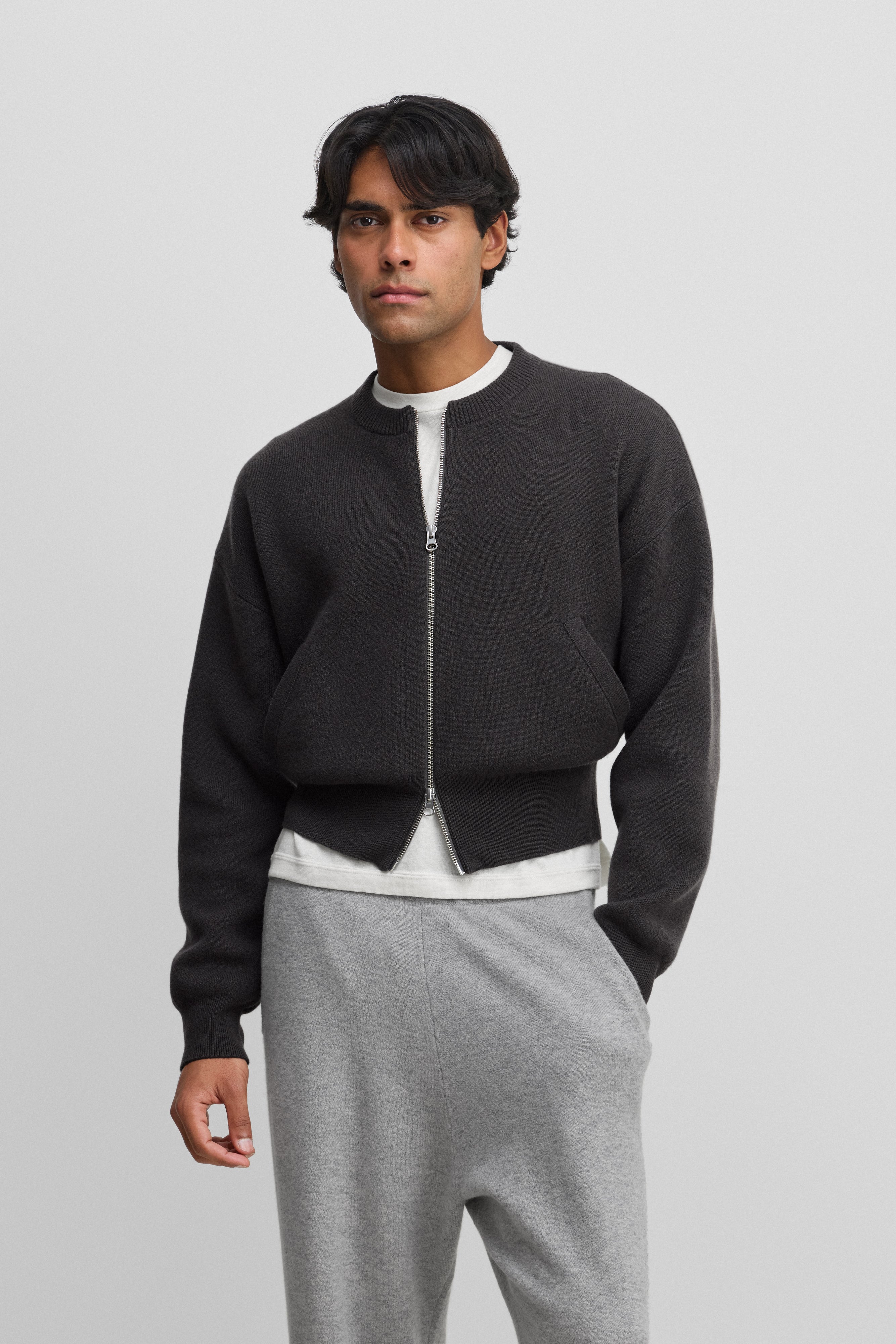 man wearing a dark grey cashmere crew-neck cardigan with a metallic two-way zipper and side pockets.