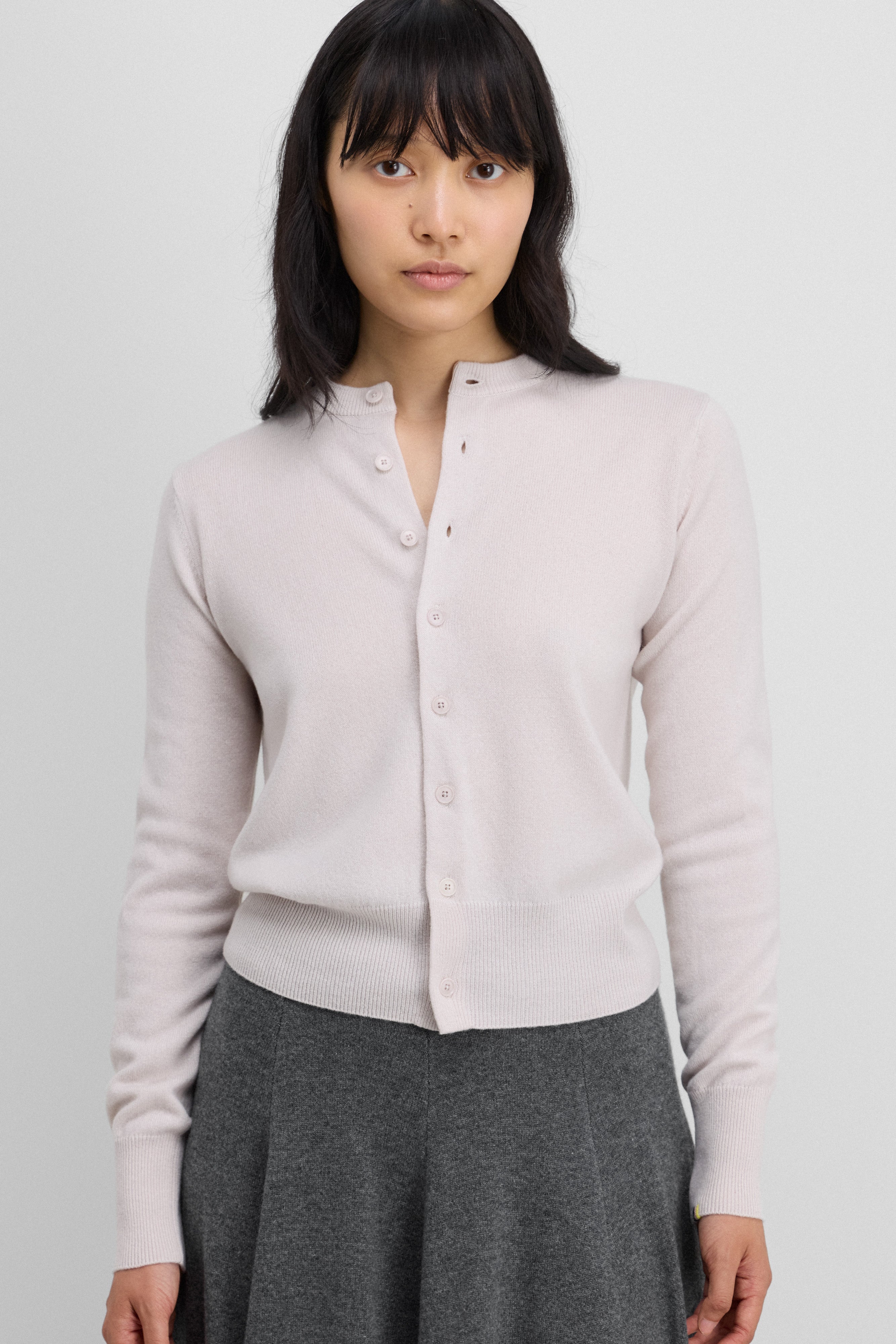 woman wearing a white cashmere crew-neck cardigan with eight corozo buttons and ribbed trims.