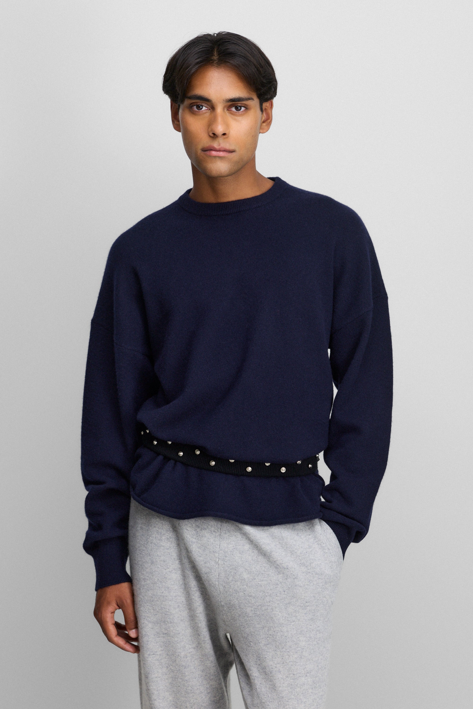 man wearing a navy blue cashmere crewneck sweater with a curved hem and drop shoulder.