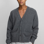 man wearing a dark grey cashmere v-neck cardigan with corozo buttons, two front pockets, and rib-knitted hem and cuffs.