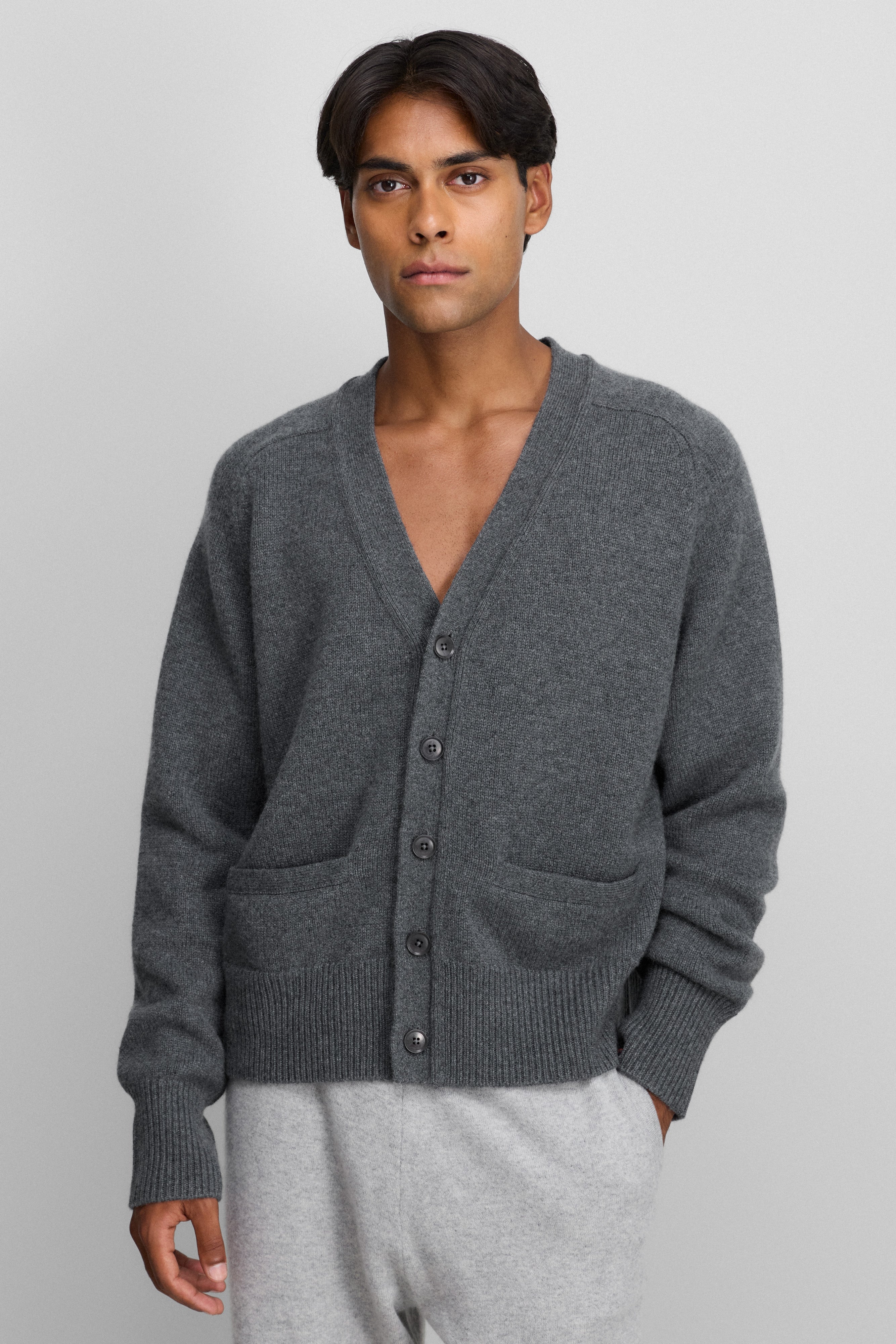 man wearing a dark grey cashmere v-neck cardigan with corozo buttons, two front pockets, and rib-knitted hem and cuffs.