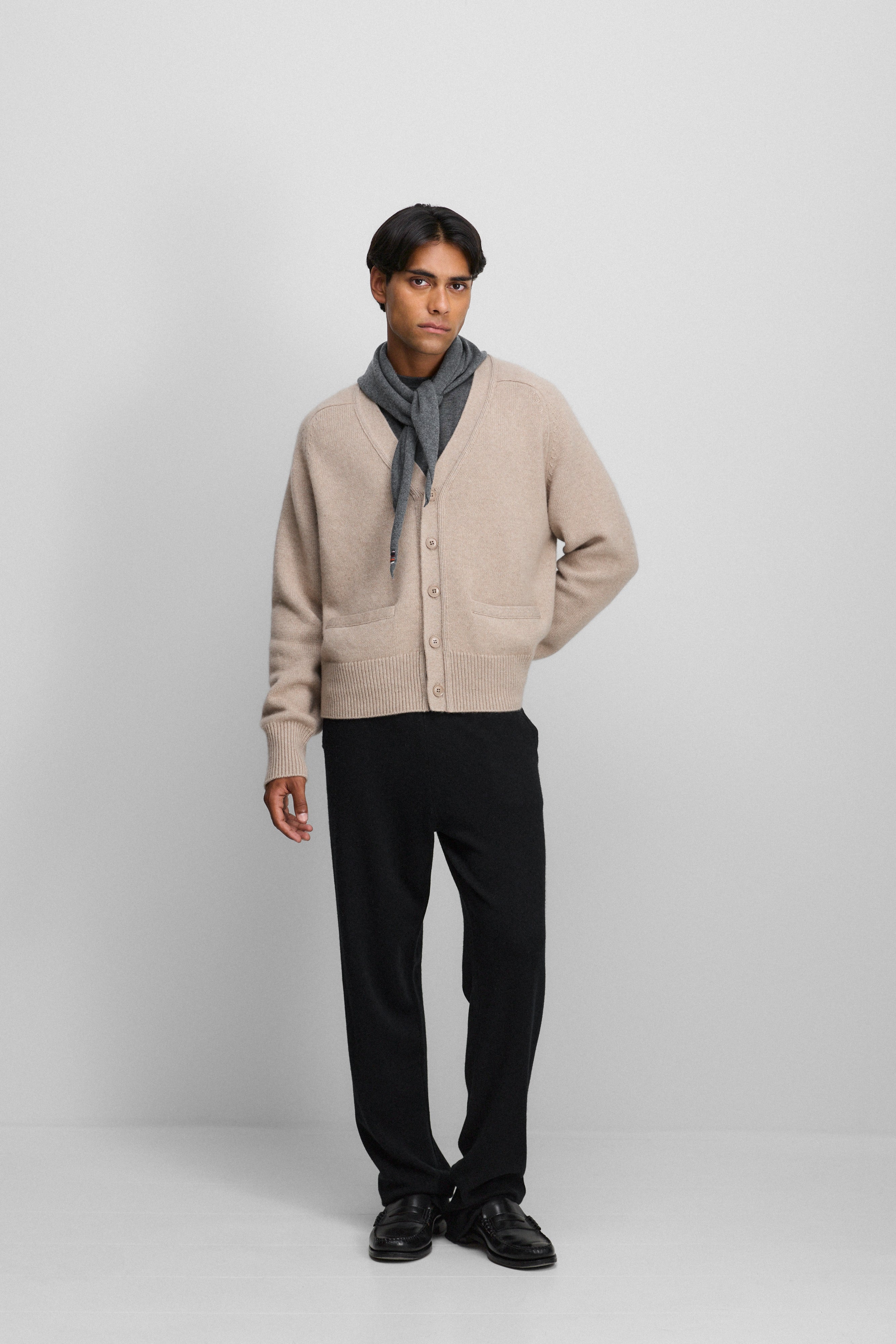 man wearing a beige cashmere v-neck cardigan with corozo button closure, styled with black cashmere pants.