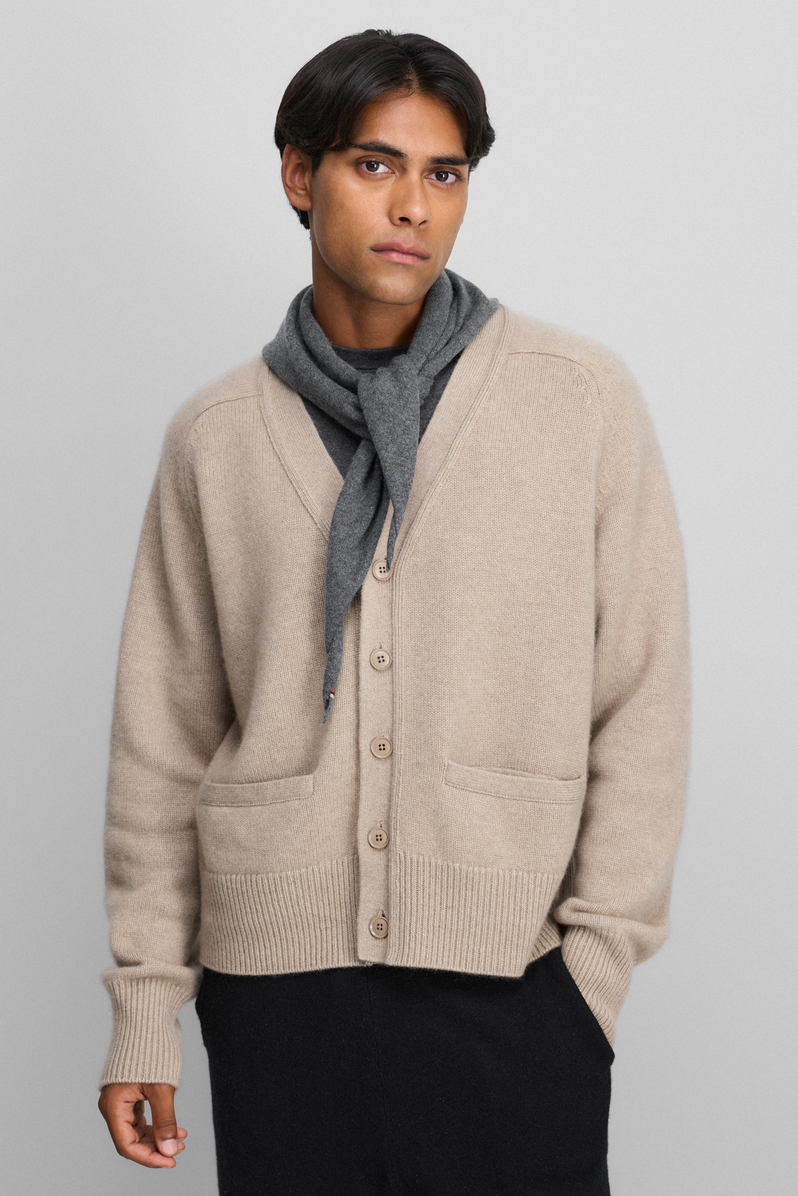 man wearing a beige heavy-knit cashmere v-neck cardigan with five corozo buttons and two front pockets.