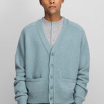 man wearing a turquoise blue cashmere v-neck cardigan with five corozo buttons and two front pockets.