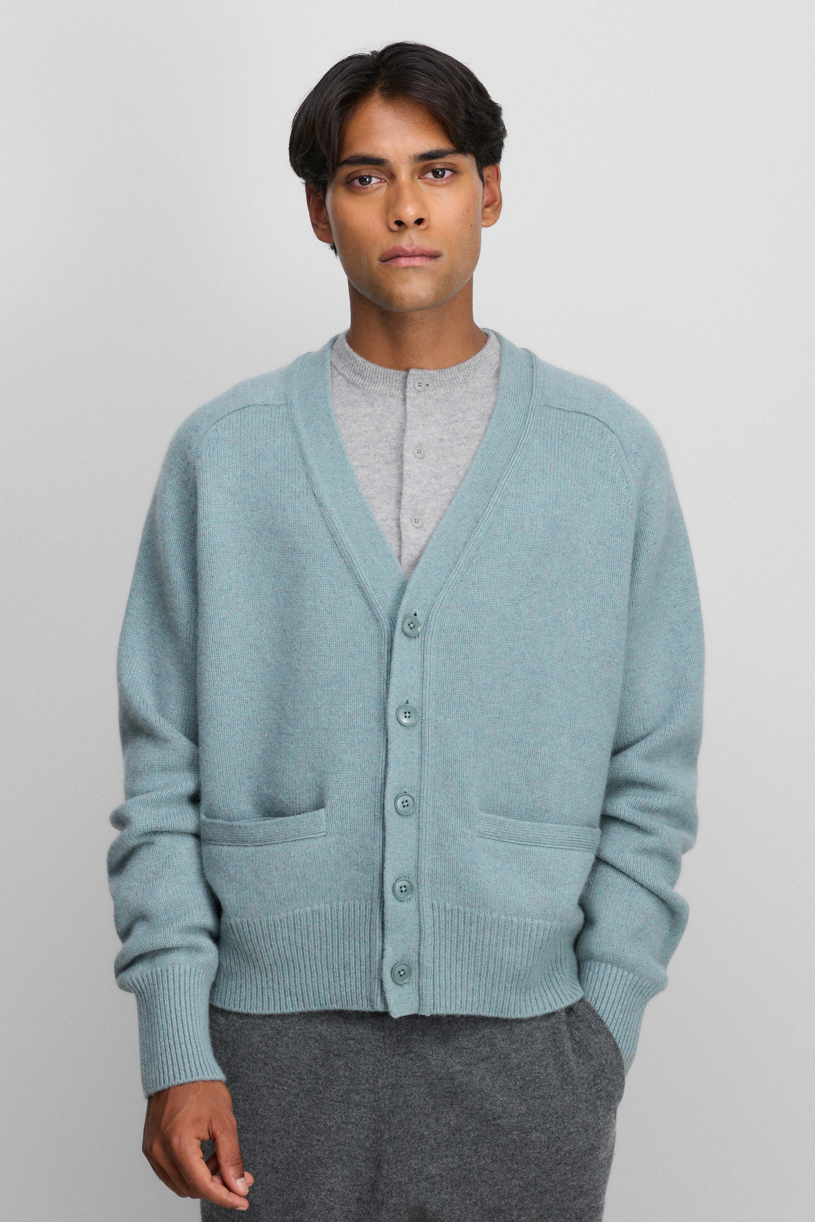 man wearing a turquoise blue cashmere v-neck cardigan with five corozo buttons and two front pockets.