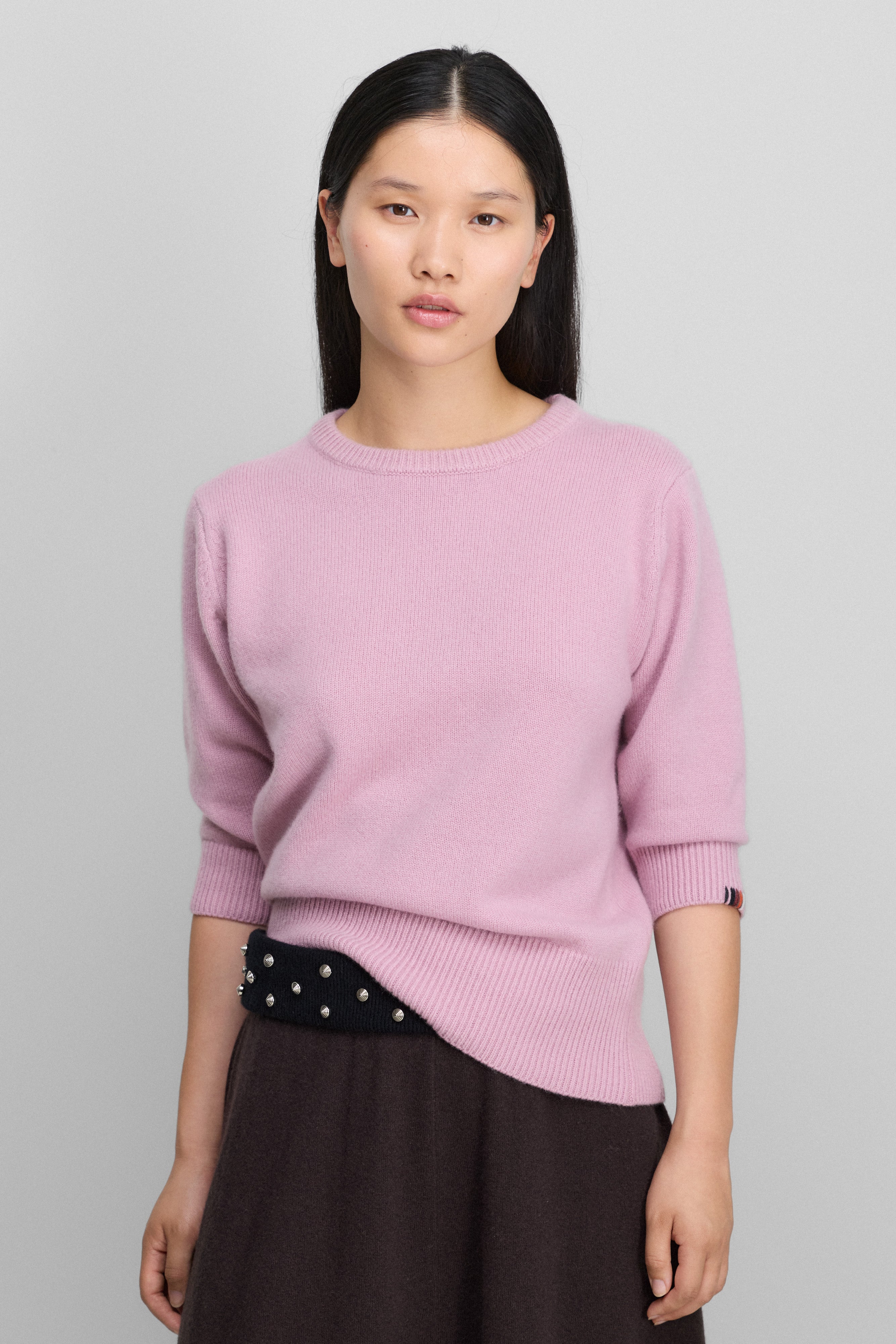 woman wearing a pink cashmere crew-neck sweater with elbow-length sleeves and ribbed neck, hem, cuffs.
