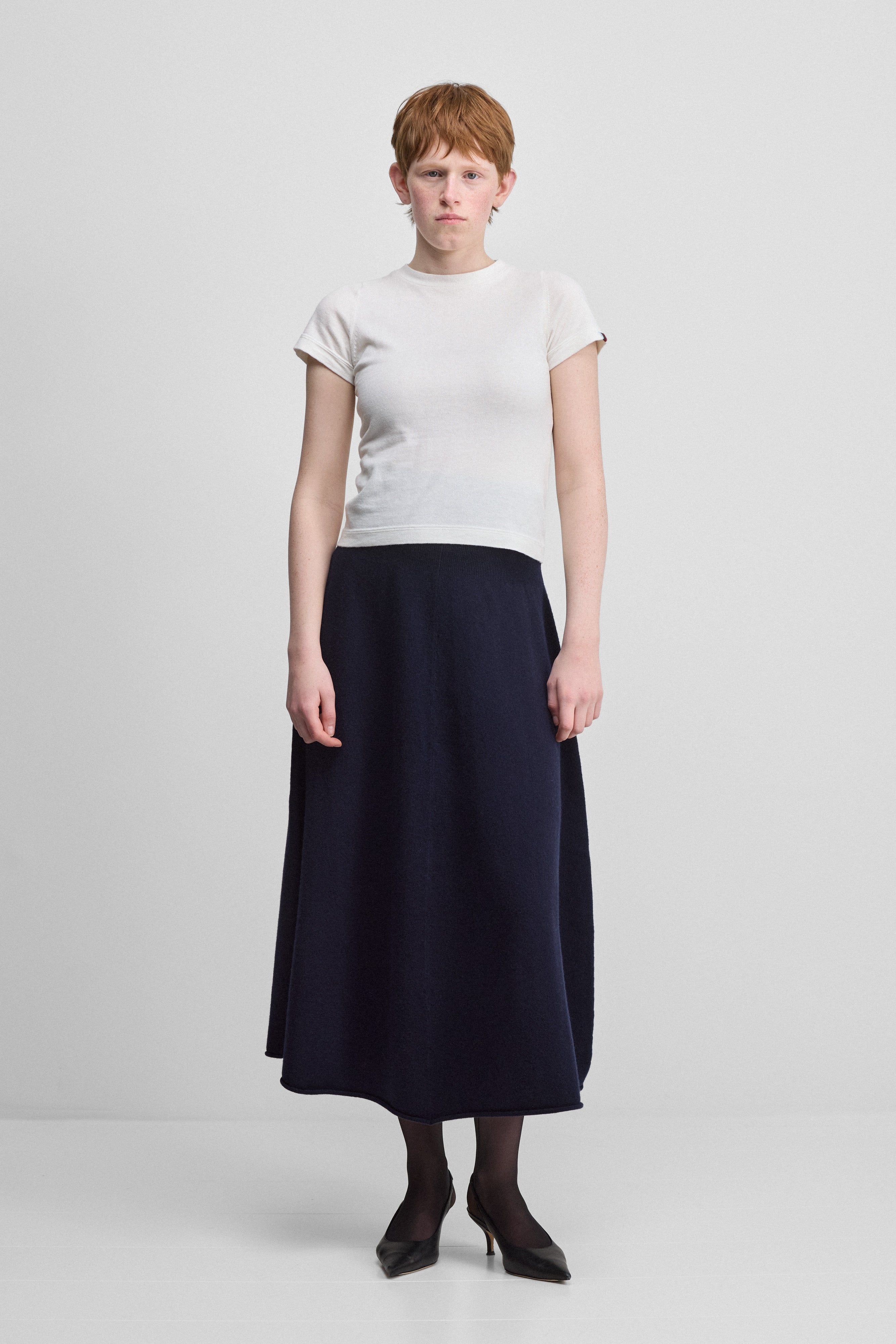 woman wearing a navy blue flared cashmere midi skirt, styled with a white t-shirt.