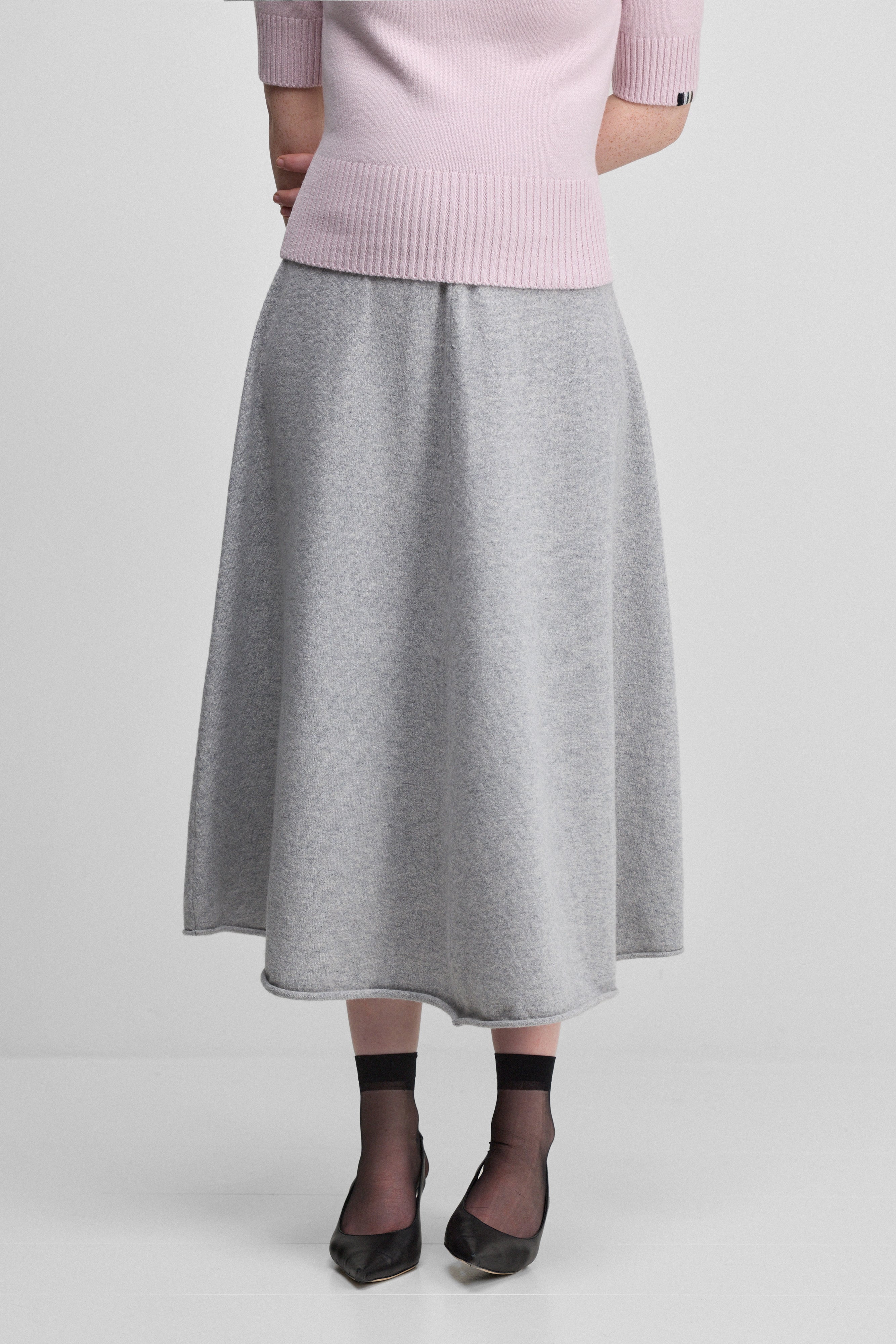 woman wearing a grey flared cashmere midi skirt with rolling edge hem.