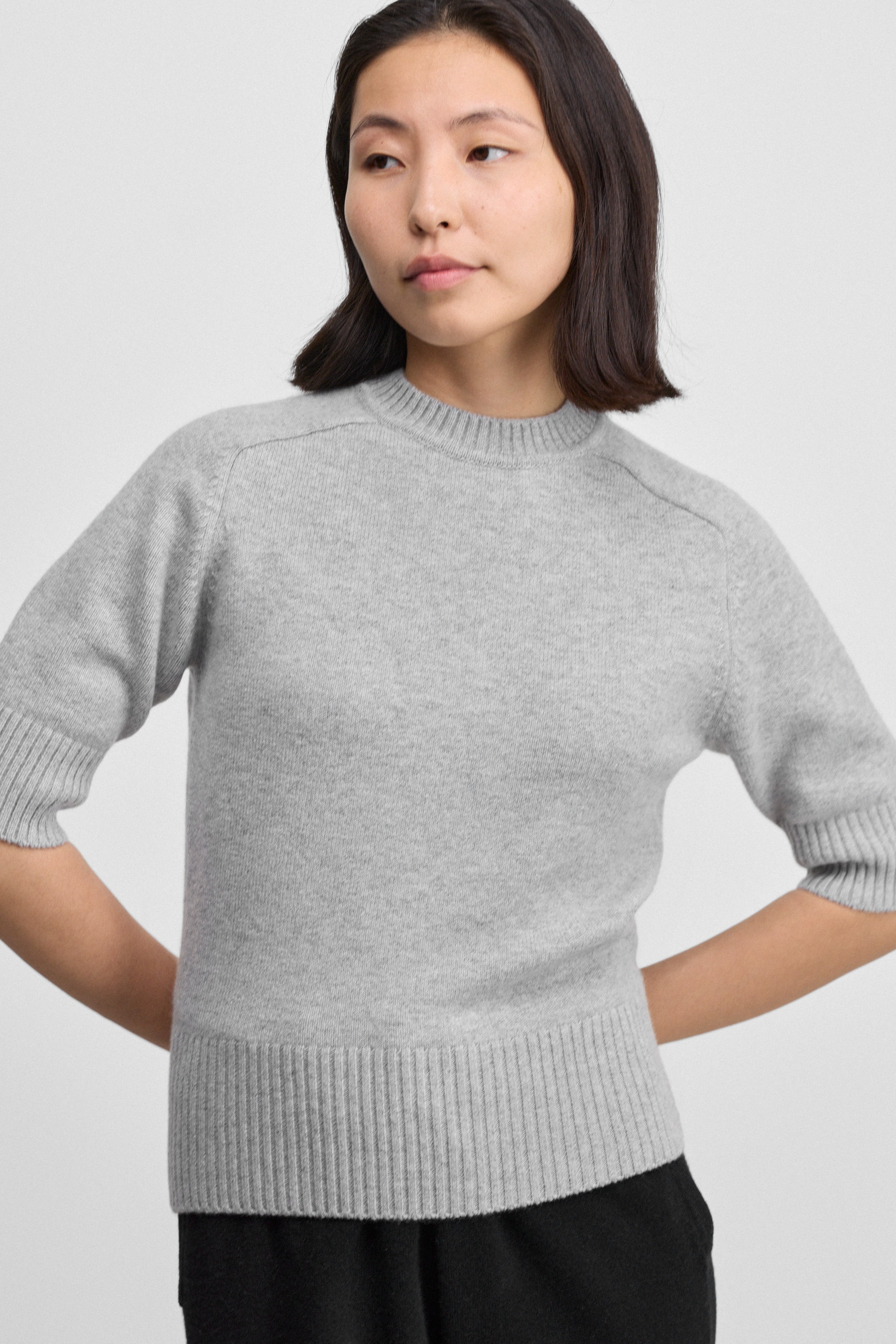 woman wearing a grey fitted crew-neck sweater with elbow-length sleeves and rib-knitted hem, cuffs, and neckline.