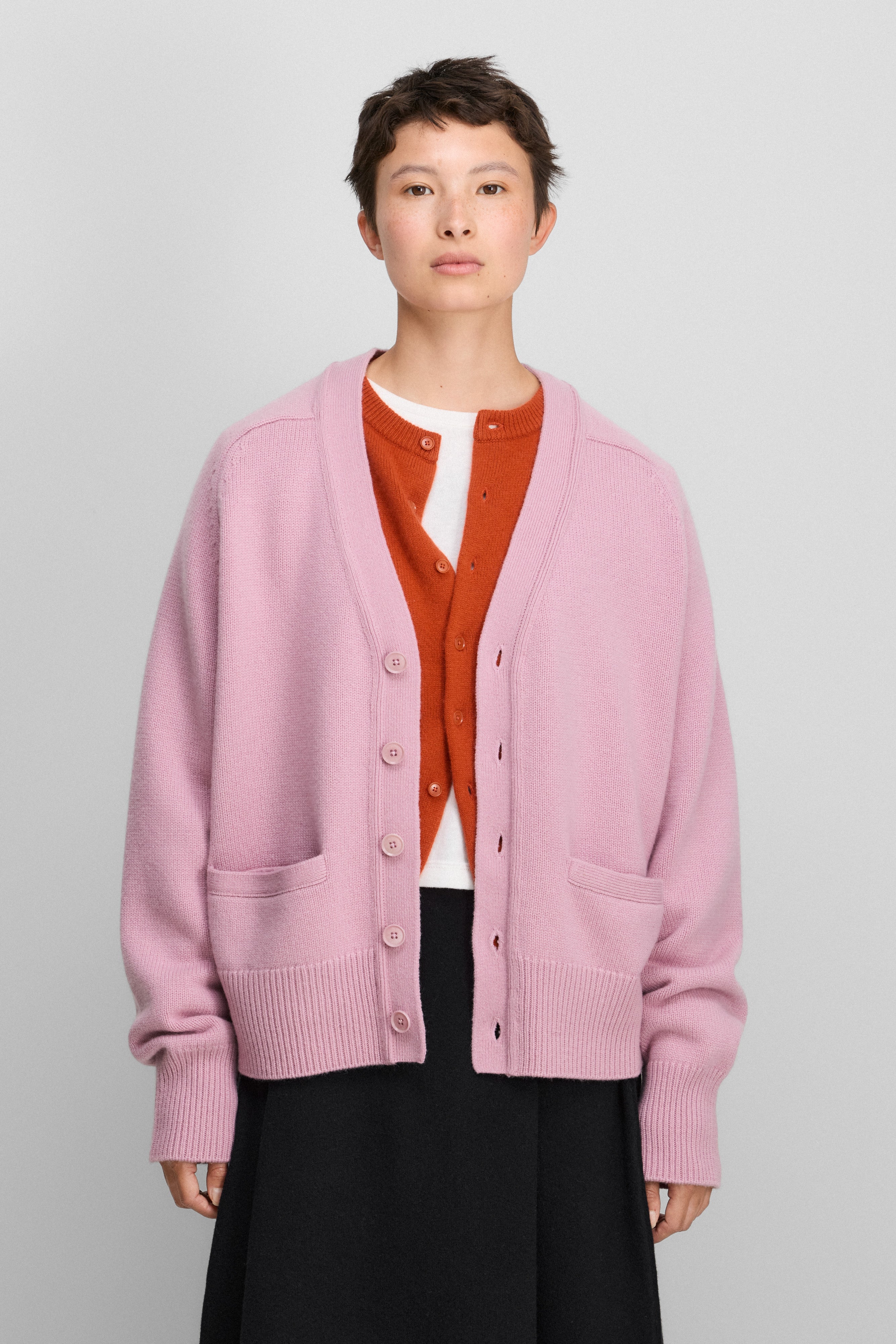 woman wearing a pink heavy-knit cashmere v-neck cardigan with five corozo buttons and two front pockets.