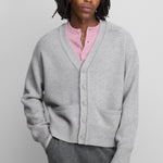man wearing a grey cashmere v-neck cardigan with five corozo buttons, two front pockets, and ribbed hem and cuffs.