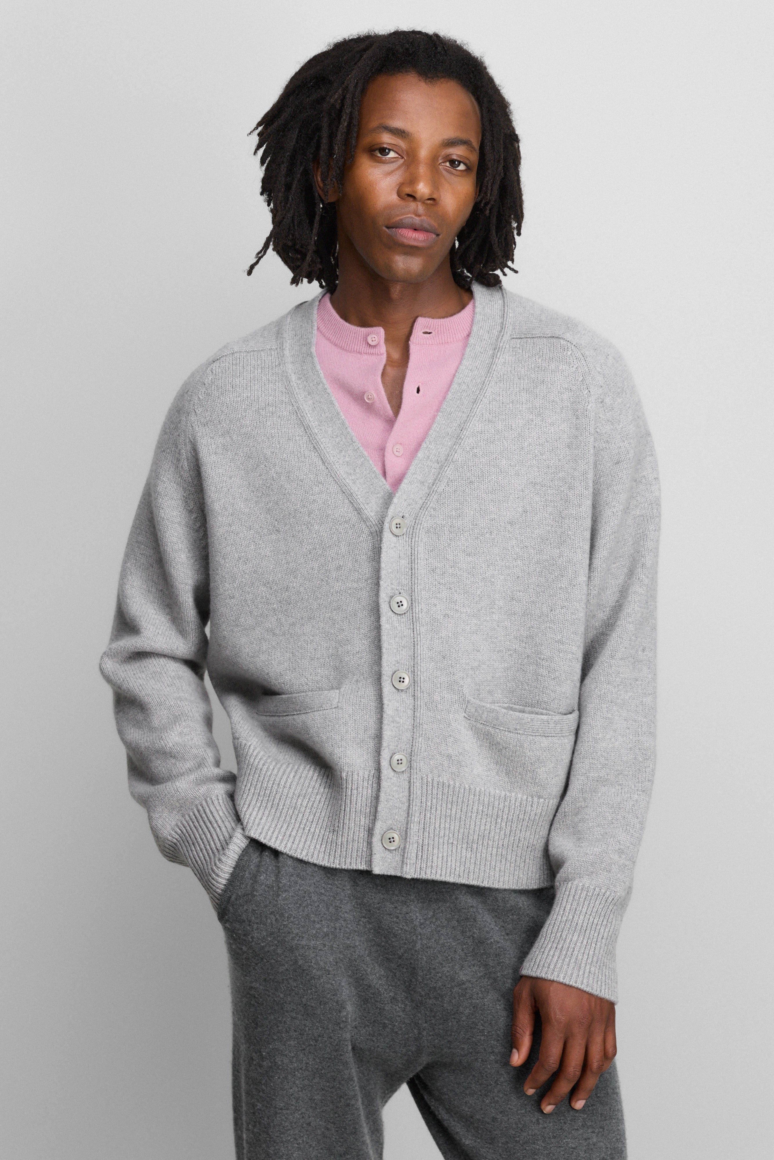 man wearing a grey cashmere v-neck cardigan with five corozo buttons, two front pockets, and ribbed hem and cuffs.