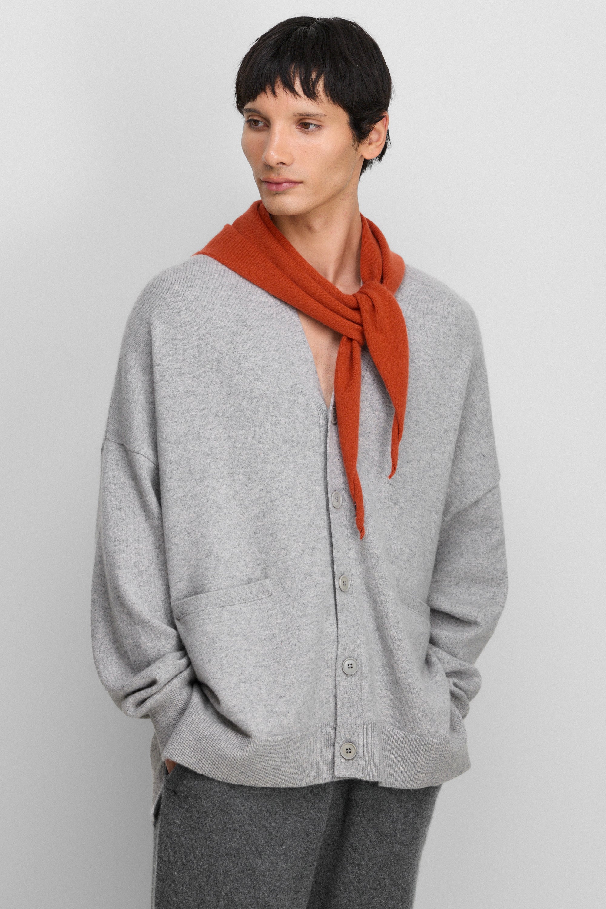 man wearing an oversized grey cashmere v-neck cardigan with five corozo buttons and two front pockets.