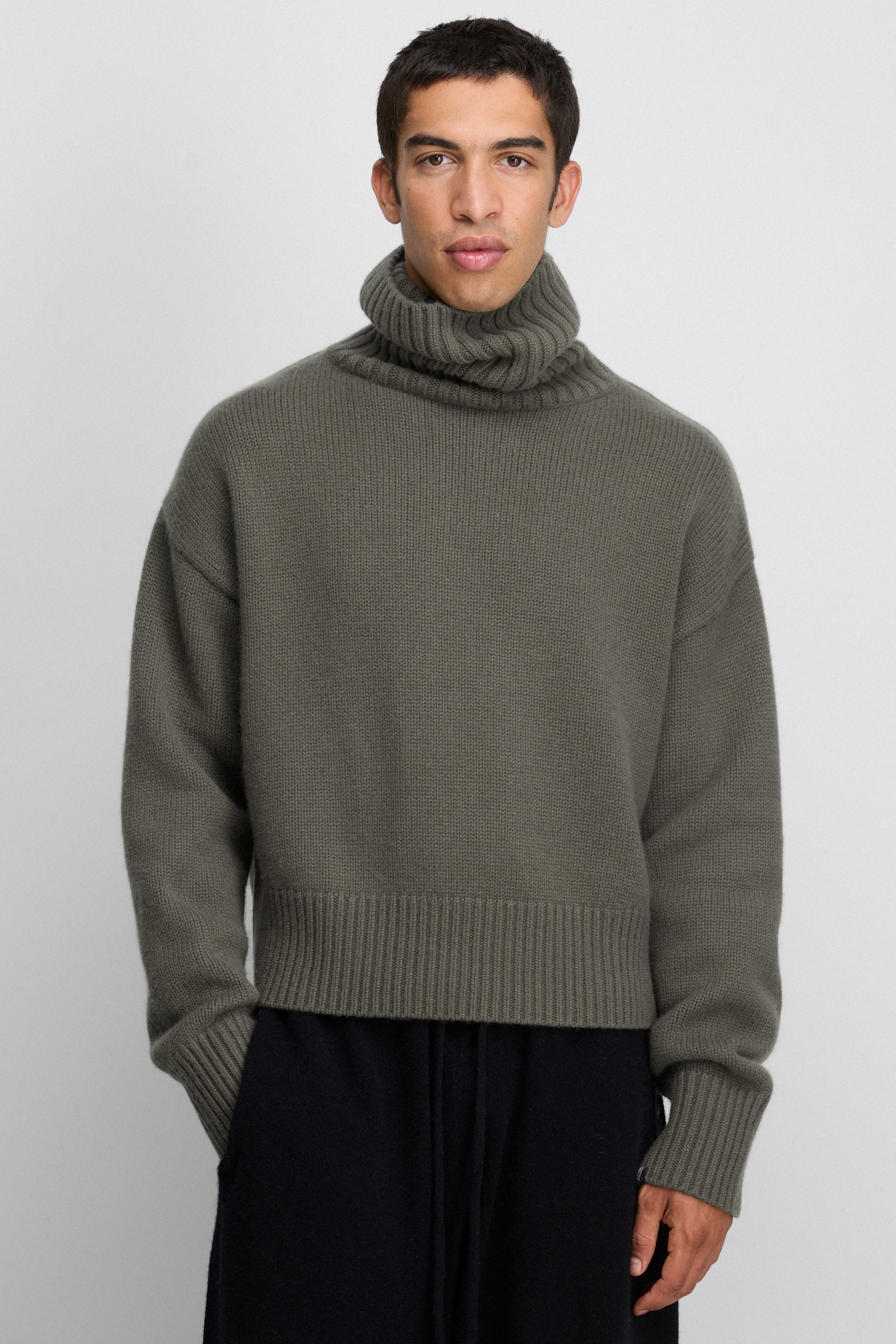 man wearing a short dark green cashmere turtleneck sweater with drop shoulder and ribbed hem, cuffs, neck.