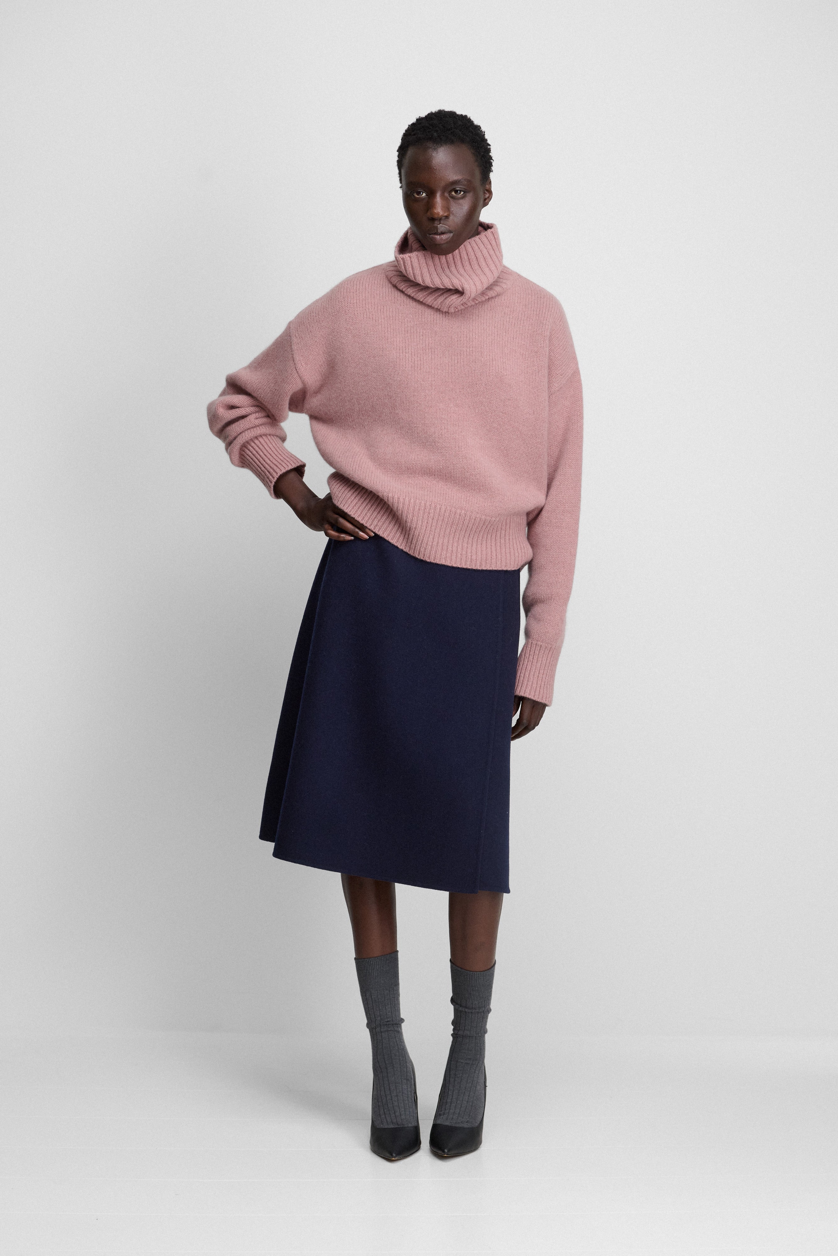 woman wearing a navy-blue double-faced midi wrap skirt with an a-line silhouette, styled with a pink sweater.