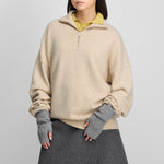 woman wearing a light beige quarter-zip cashmere sweater with drop shoulder and ribbed hem and cuffs.