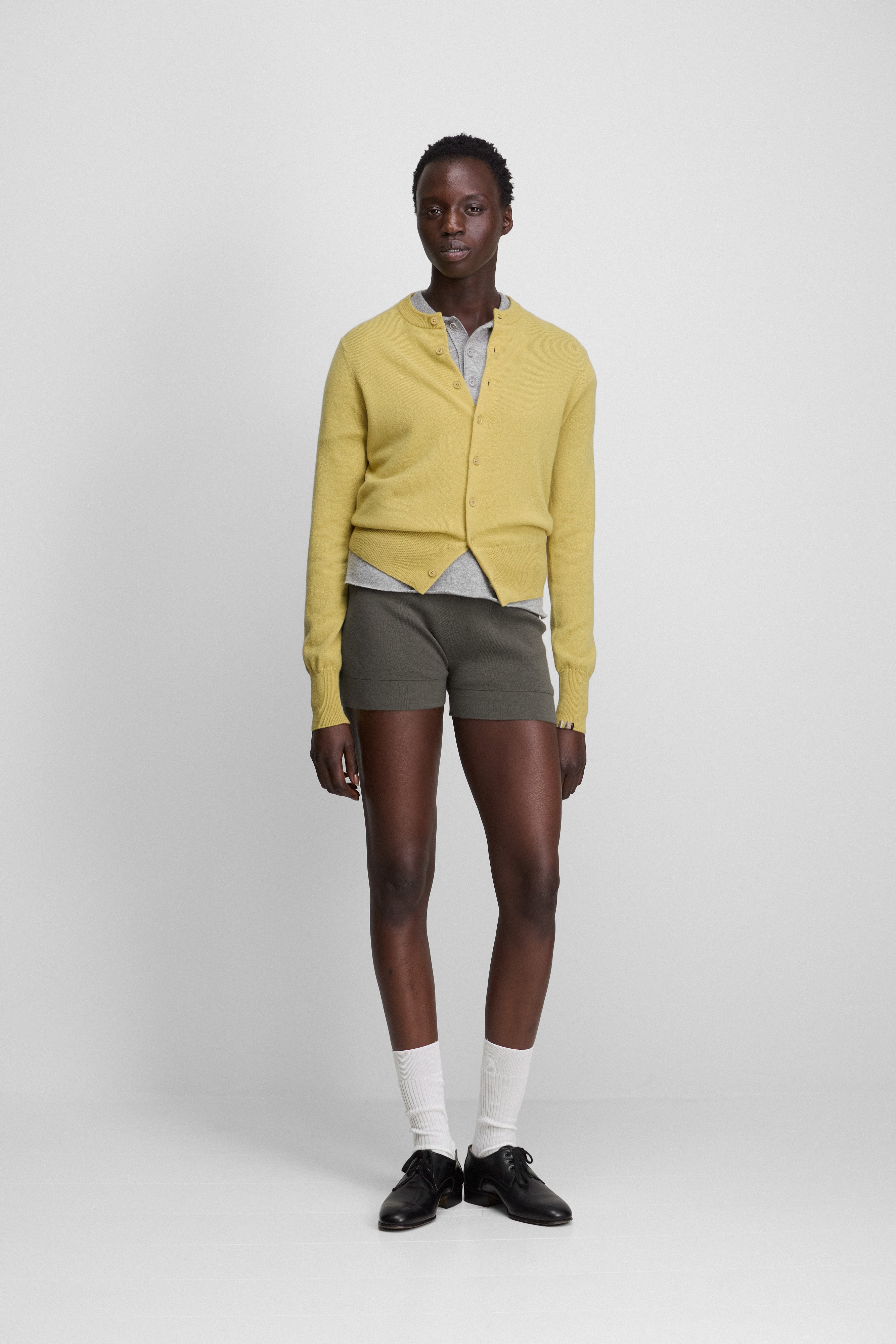 woman wearing fitted army green cotton cashmere rib-knit shorts, styled with a yellow cardigan.