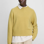 woman wearing a yellow heavy-knit cashmere crew-neck sweater with saddle shoulder and ribbed trims.