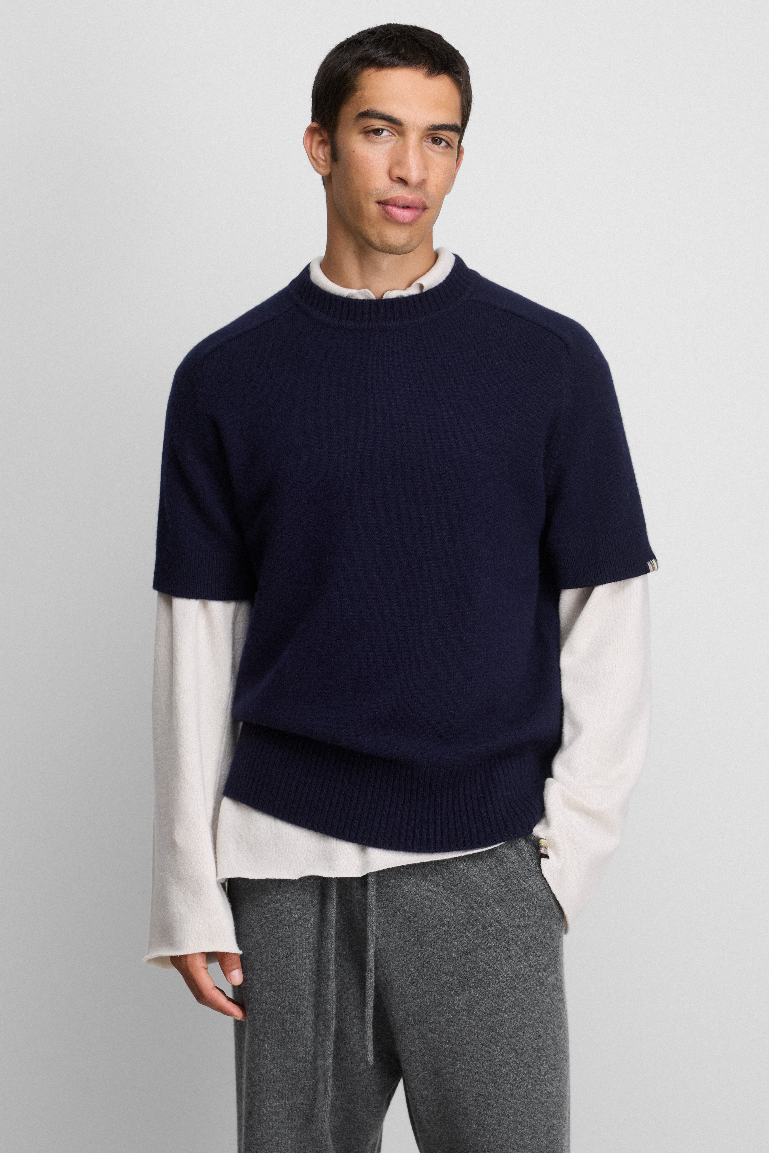 man wearing a navy blue cashmere crew-neck sweater with short sleeves, styled over a white sweater.