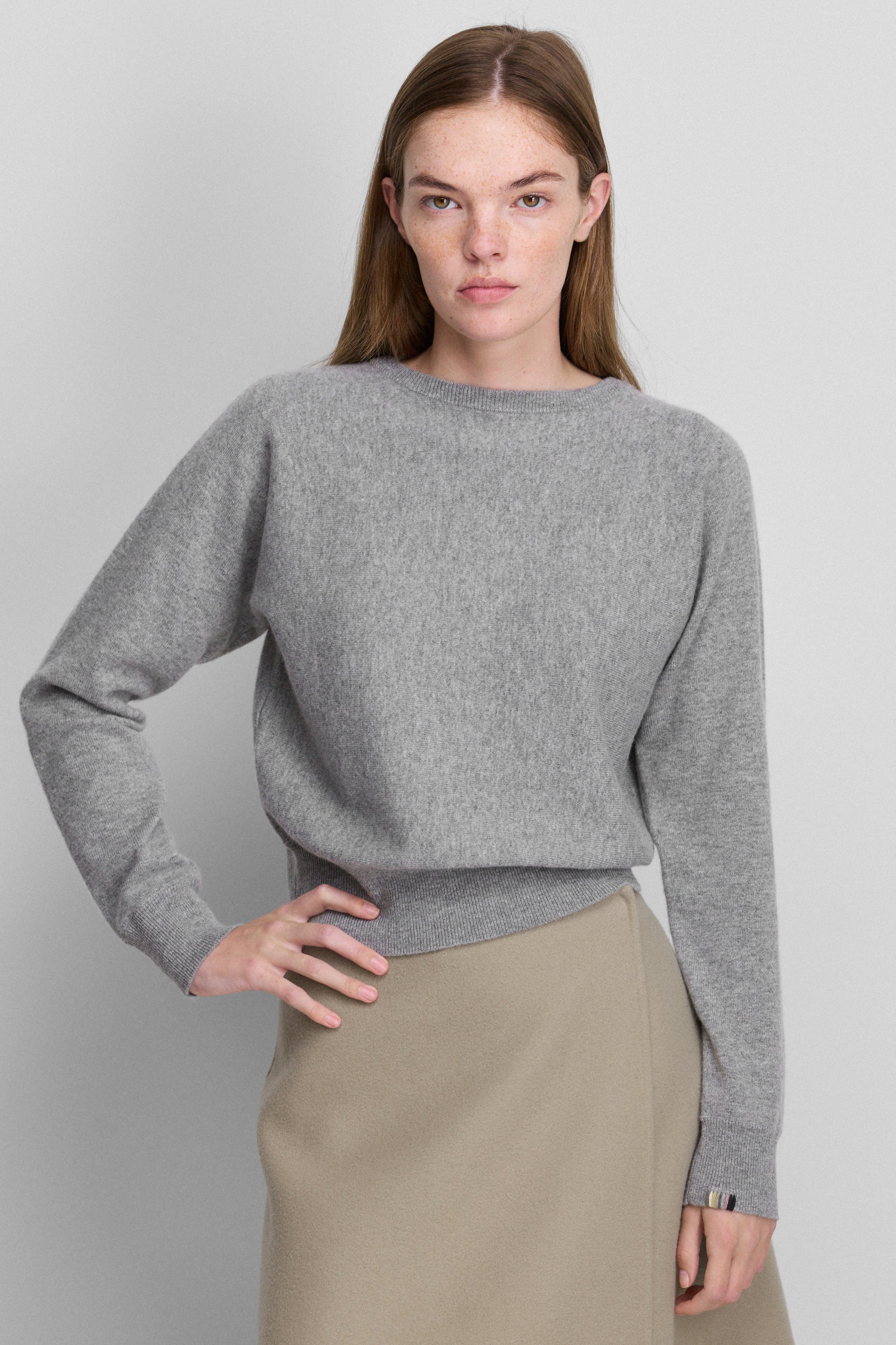 woman wearing a grey cashmere crew-neck sweater with bat sleeves and ribbed hem.