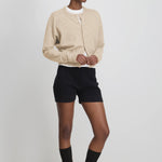 woman wearing fitted black cotton cashmere rib-knit shorts, styled with a beige cardigan.