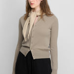 woman wearing a beige cashmere crew-neck cardigan with eight corozo buttons and ribbed trims.
