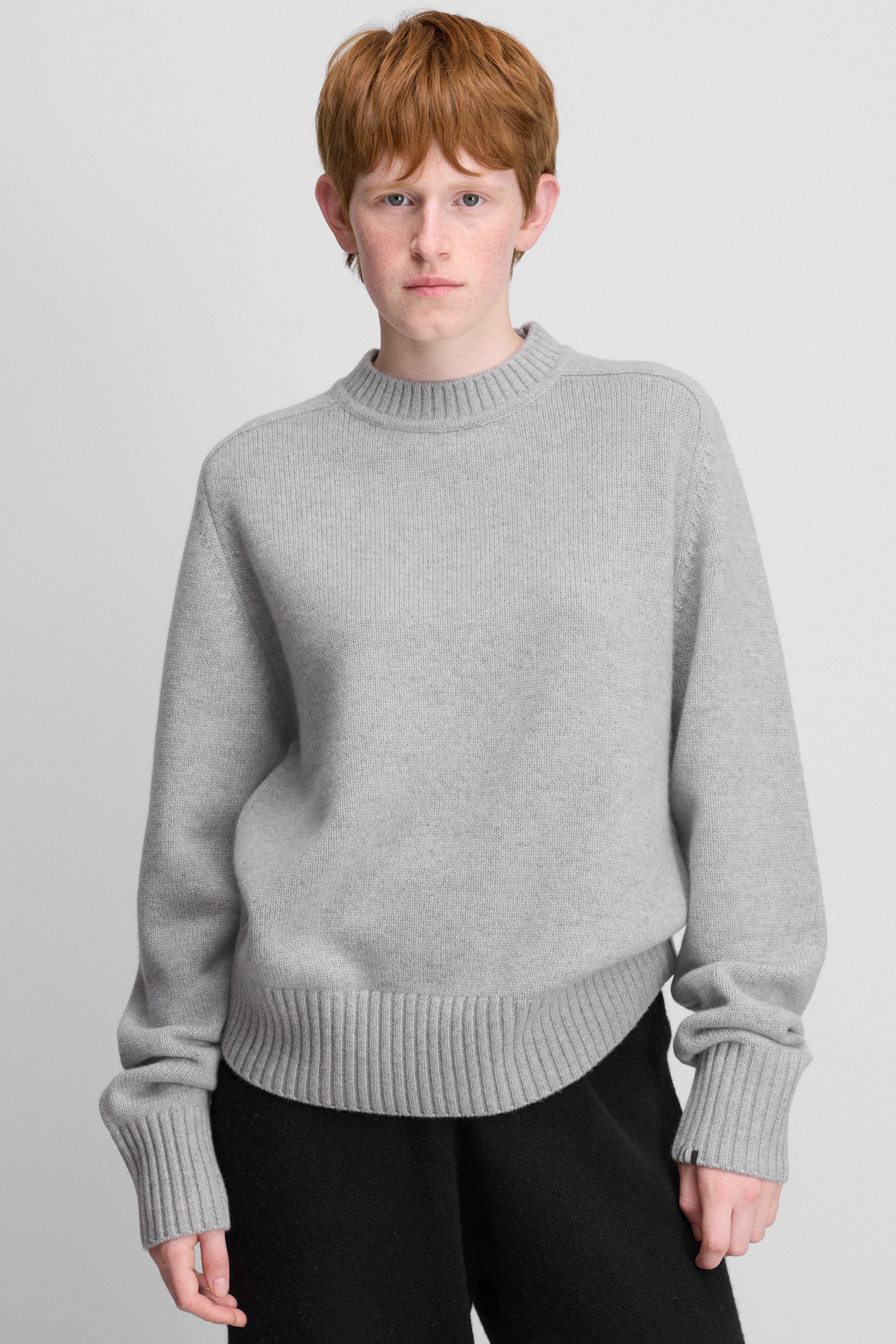 woman wearing a light grey cashmere crew-neck sweater with a saddle shoulder and ribbed trims.