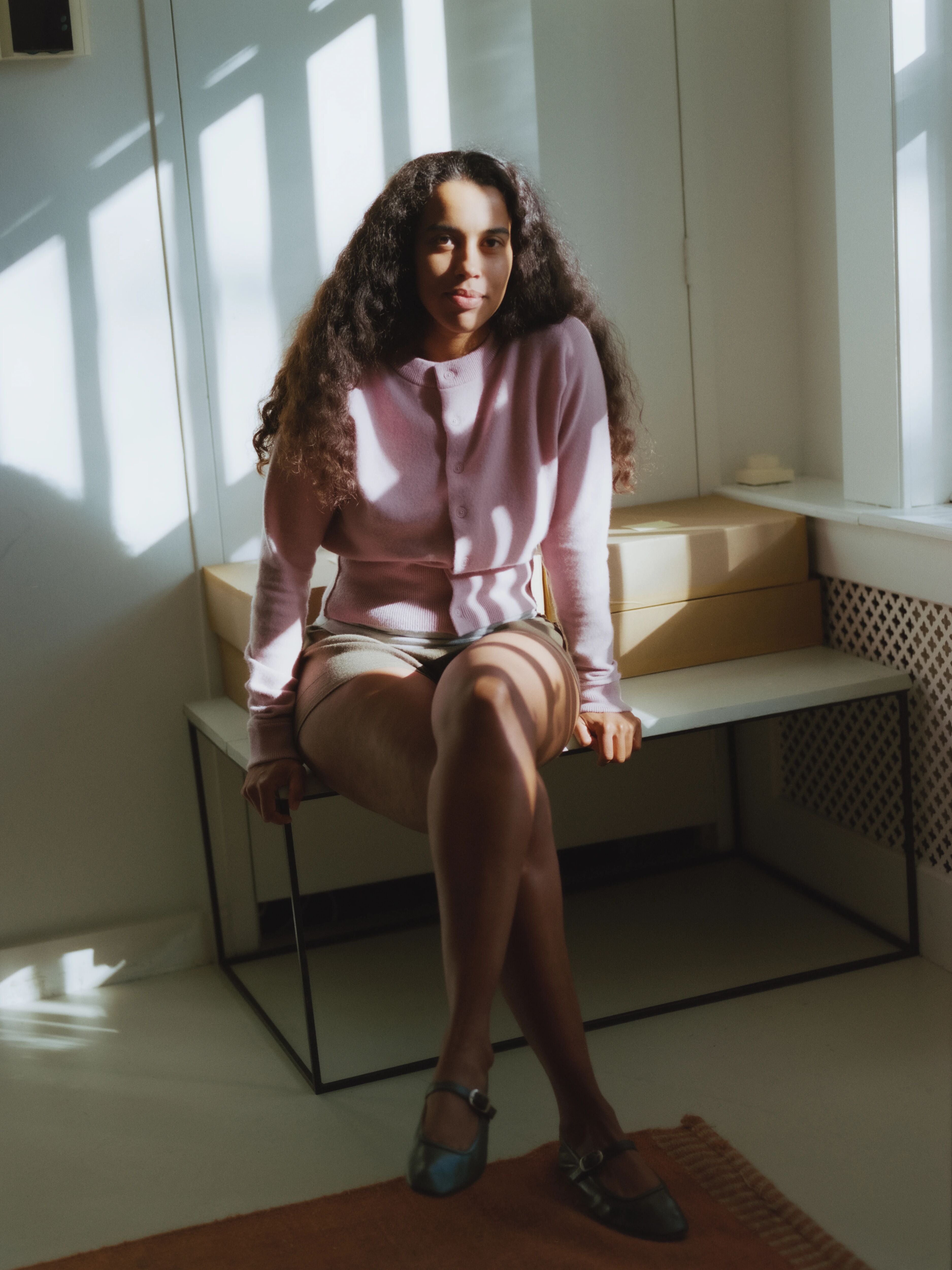 woman in a light pink cashmere button-up cardigan sitting on a bench.