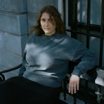 woman sitting on a bench, wearing an oversized dark grey cashmere crew-neck sweater.