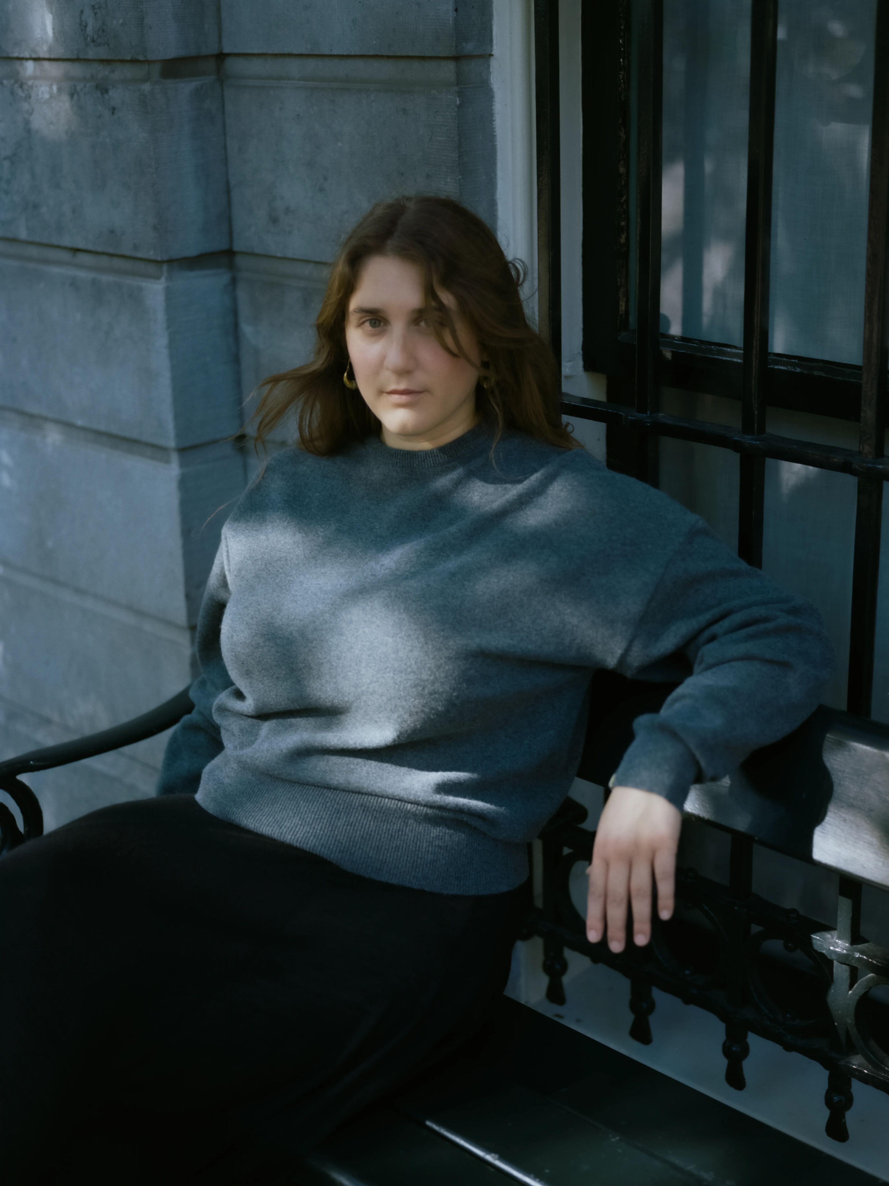 woman sitting on a bench, wearing an oversized dark grey cashmere crew-neck sweater.