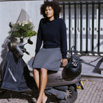 woman wearing a navy blue cashmere crewneck sweater, sitting on a motor scooter outside.