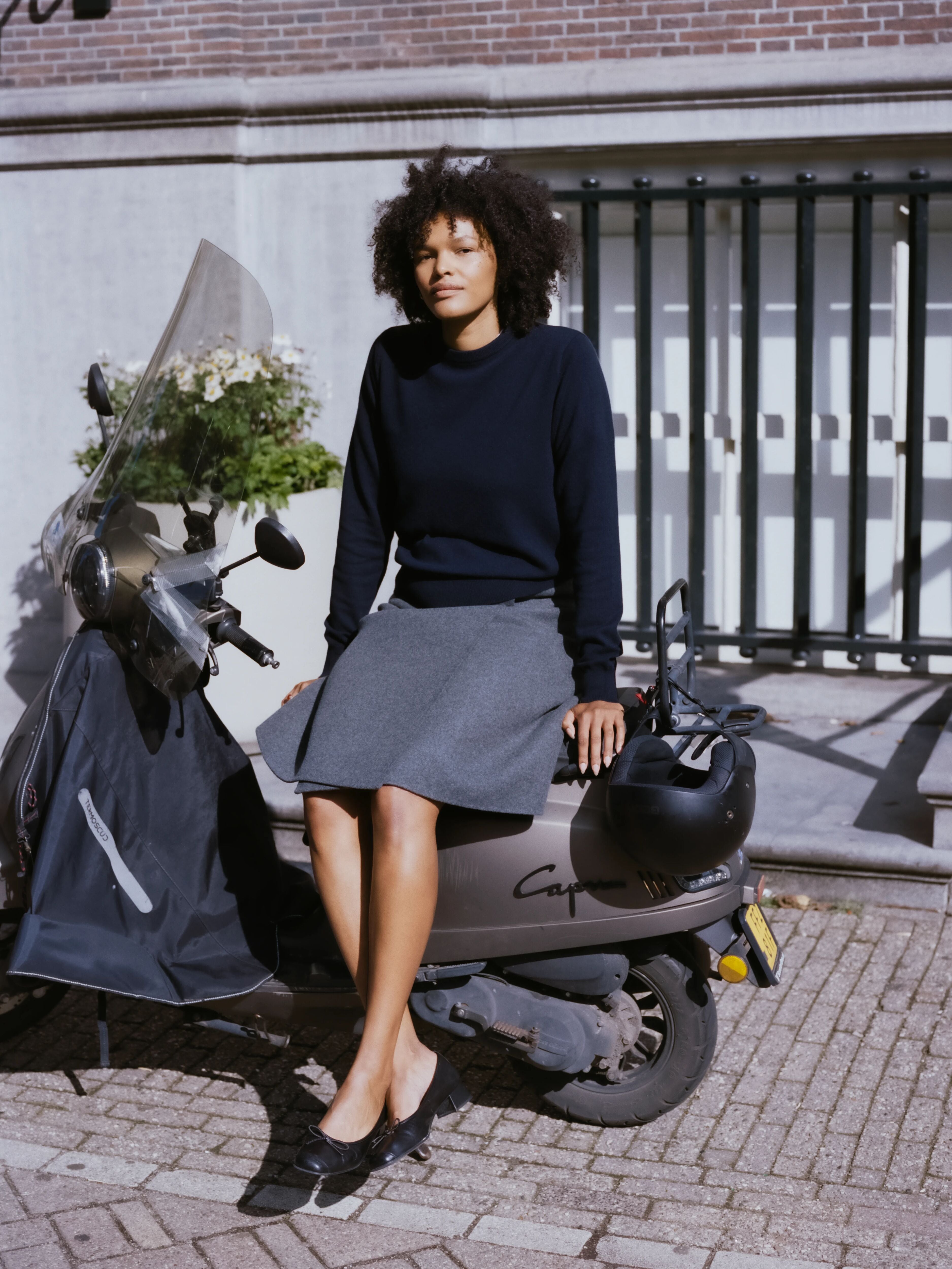 woman wearing a navy blue cashmere crewneck sweater, sitting on a motor scooter outside.