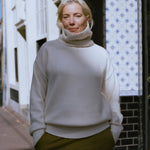 woman wearing a cream heavy-knit cashmere turtleneck sweater with ribbed trims, standing outdoors.